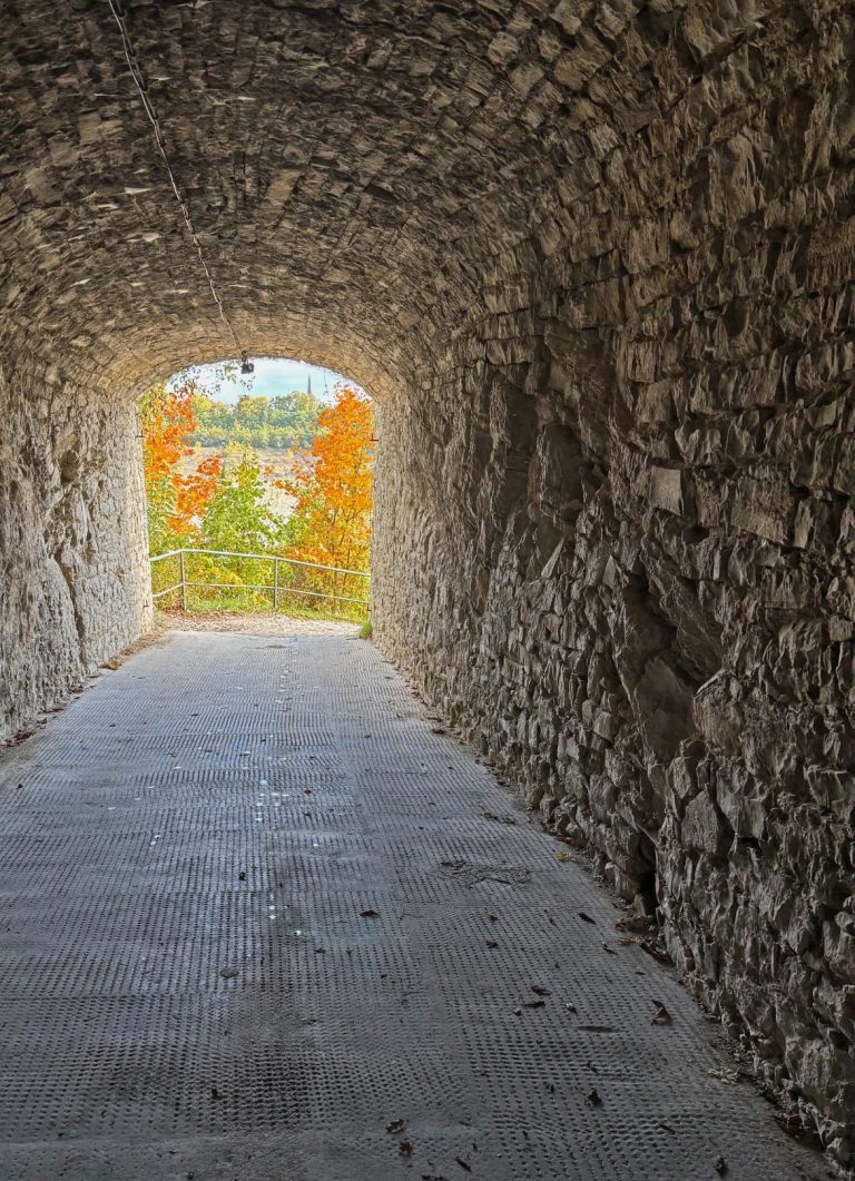 Steiniger Tunnel mit Blick auf einen farbenfrohen herbstlichen Außenbereich.